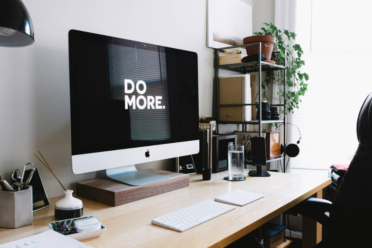 Aufgeräumter Schreibtisch mit iMac, auf dessen Bildschirm «DO MORE.» steht