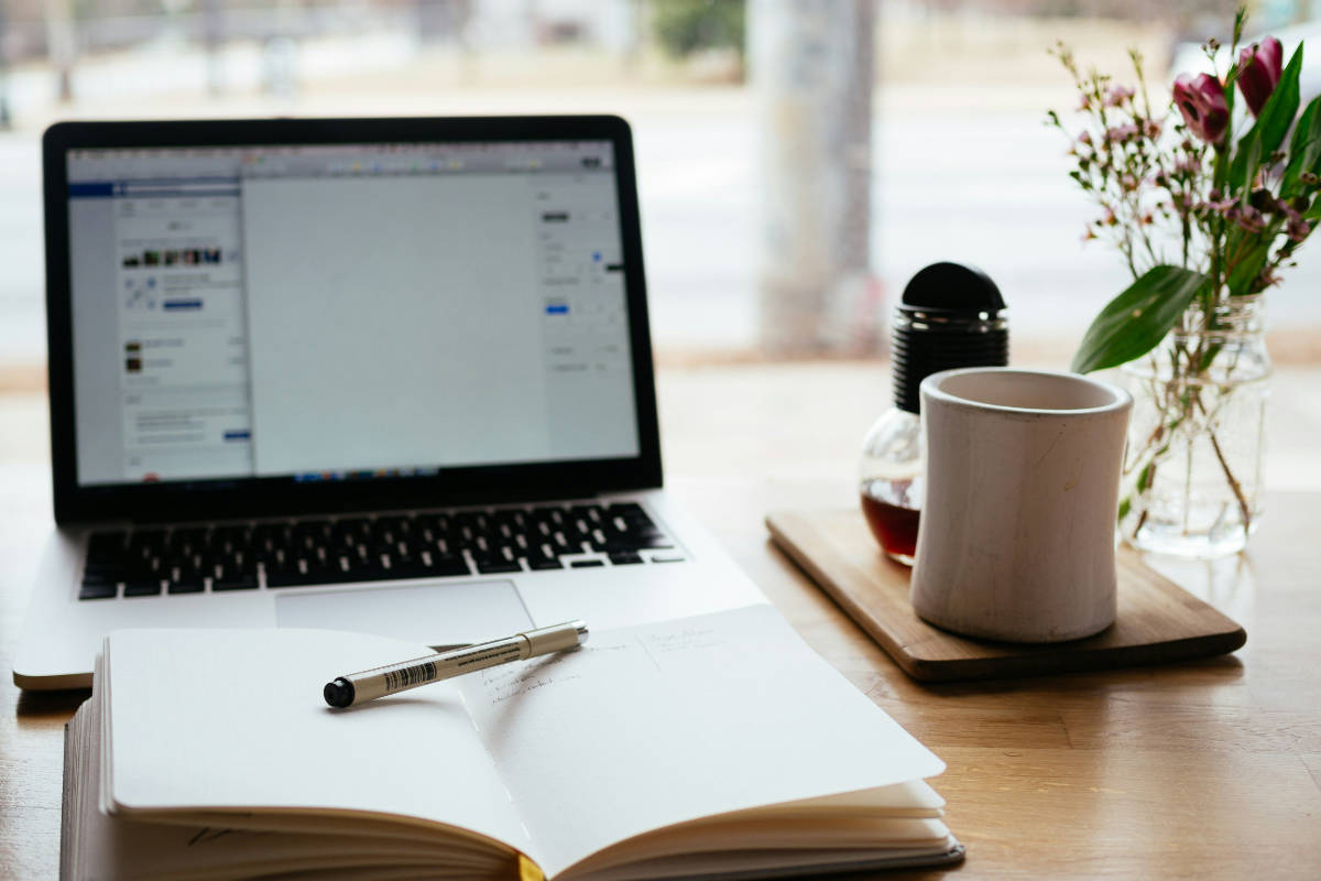 Laptop mit offenem Notizbuch und Kaffee – Website-Texte schreiben